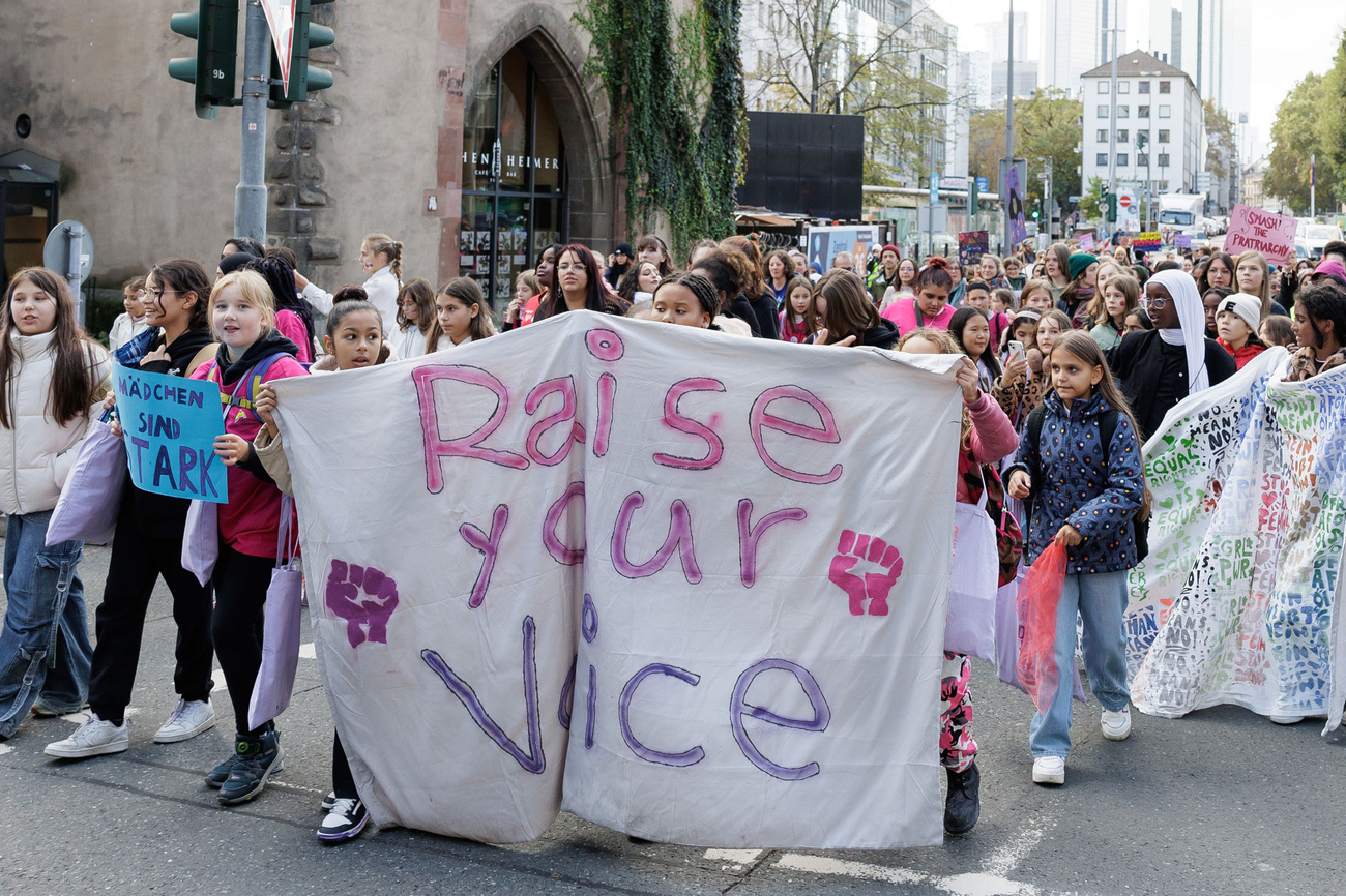 Junge Frauen laufen auf einer Demo hinter einem Transparent mit der Aufschrift: Raise your voice