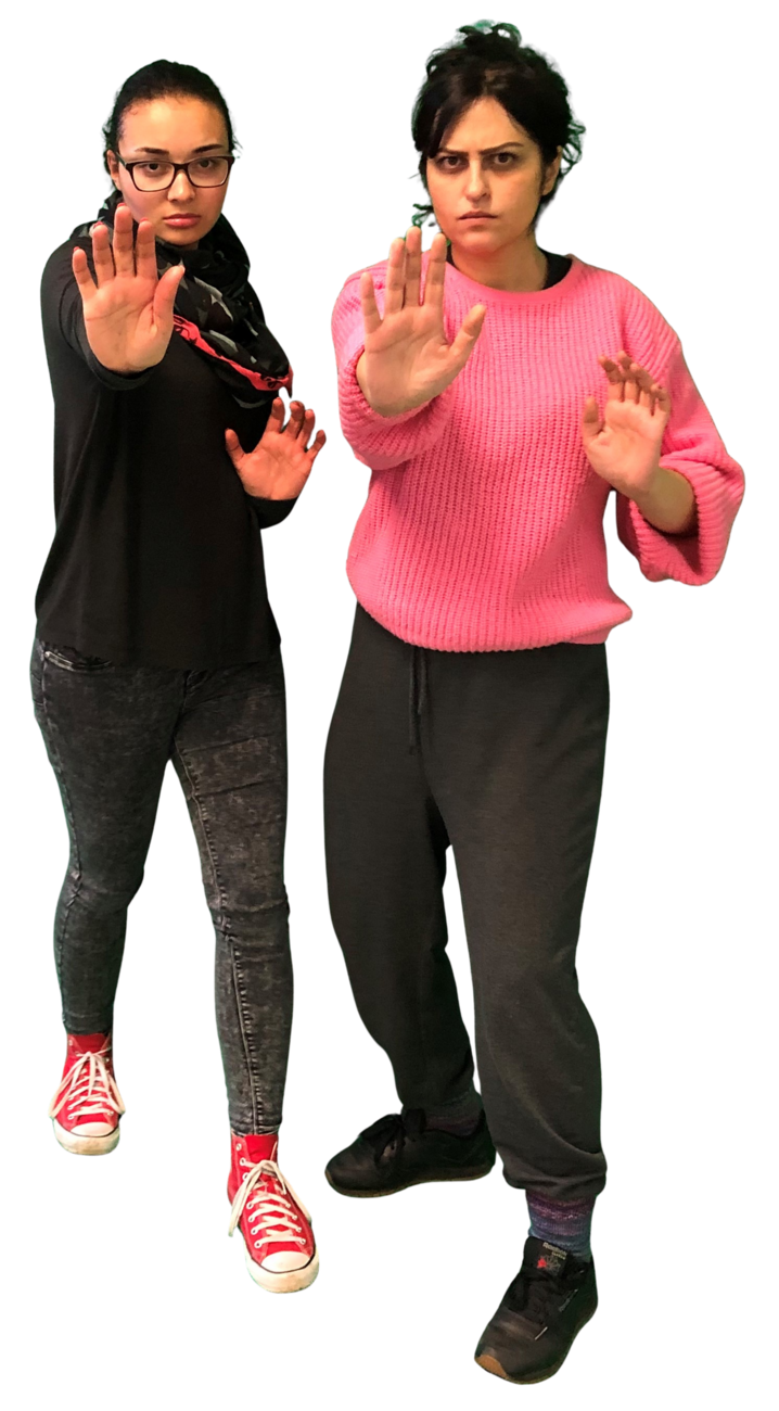 Zwei Frauen stehen aufrecht. Ihre Körper sind mit einer verteidigenden Haltung in die Kamera gedreht. Beide haben ihre Hände erhoben und einen abwehrenden Gesichtsausdruck